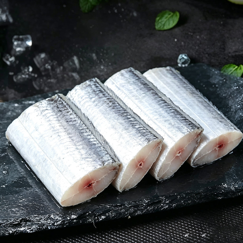 Four thick raw beltfish sections arranged on dark slate with herbs
