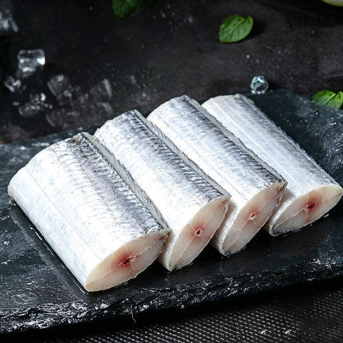 Four thick raw beltfish sections arranged on dark slate with herbs