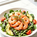 Cooked pink shrimp arranged over an avocado salad