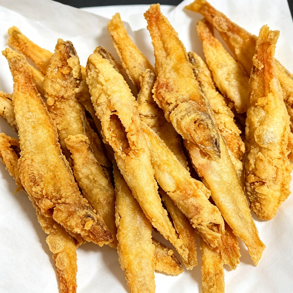 Golden deep-fried sillago pieces stacked on a white plate